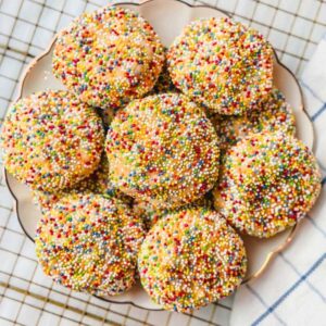 Sprinkle sugar cookies on a plate on top of a wire rack next to a blue striped kitchen towel.