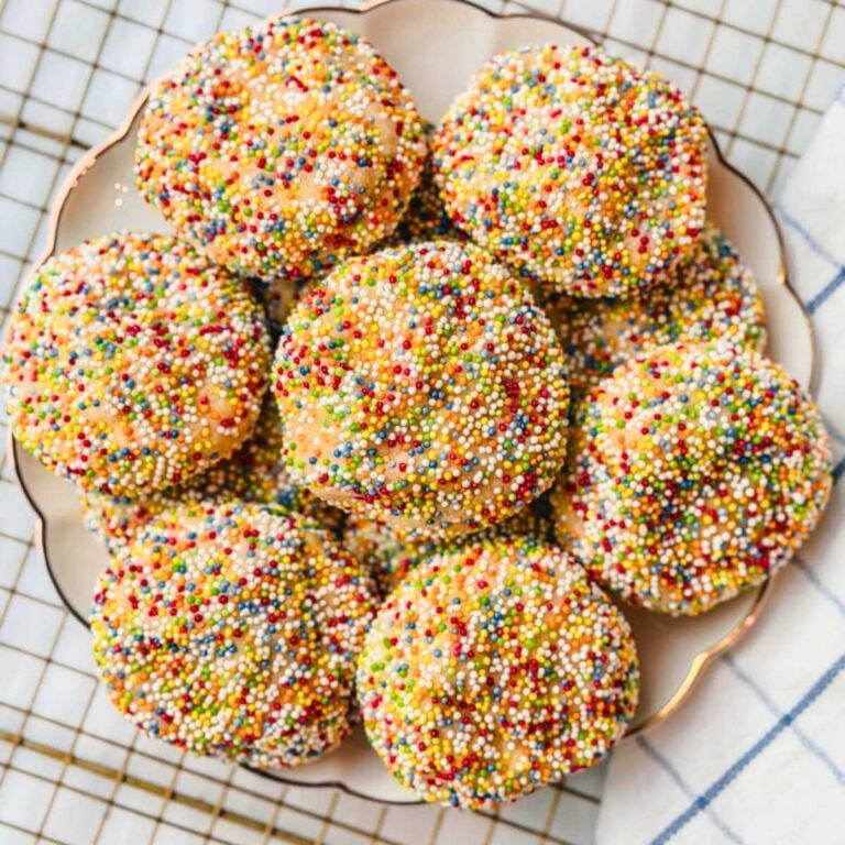 Sprinkle sugar cookies on a plate on top of a wire rack next to a blue striped kitchen towel.