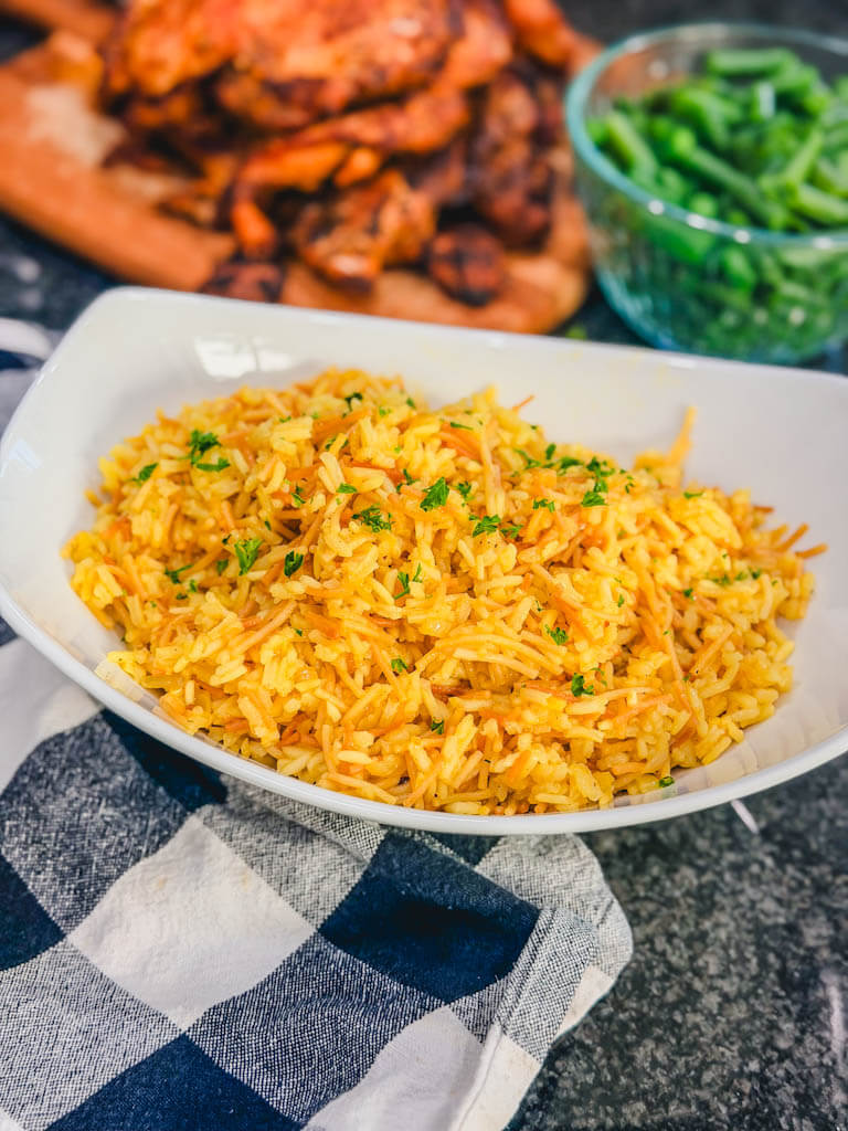 Homemade rice pilaf served with roasted chicken and green beans in the background.