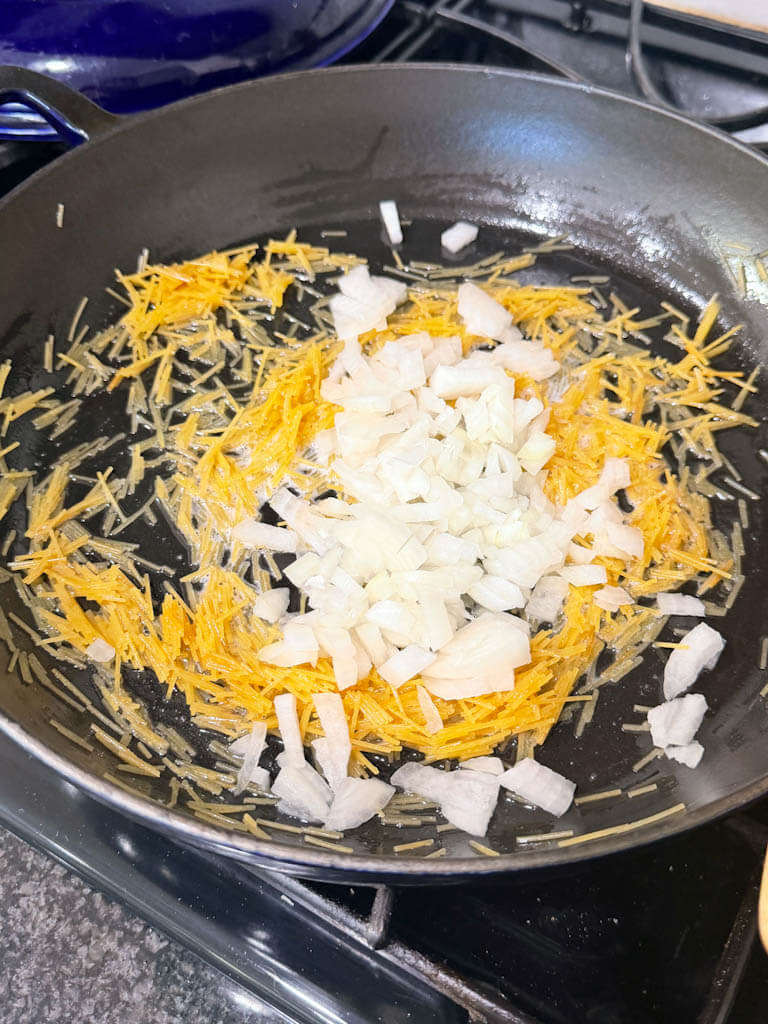 Diced onion added to toasted vermicelli in a skillet.