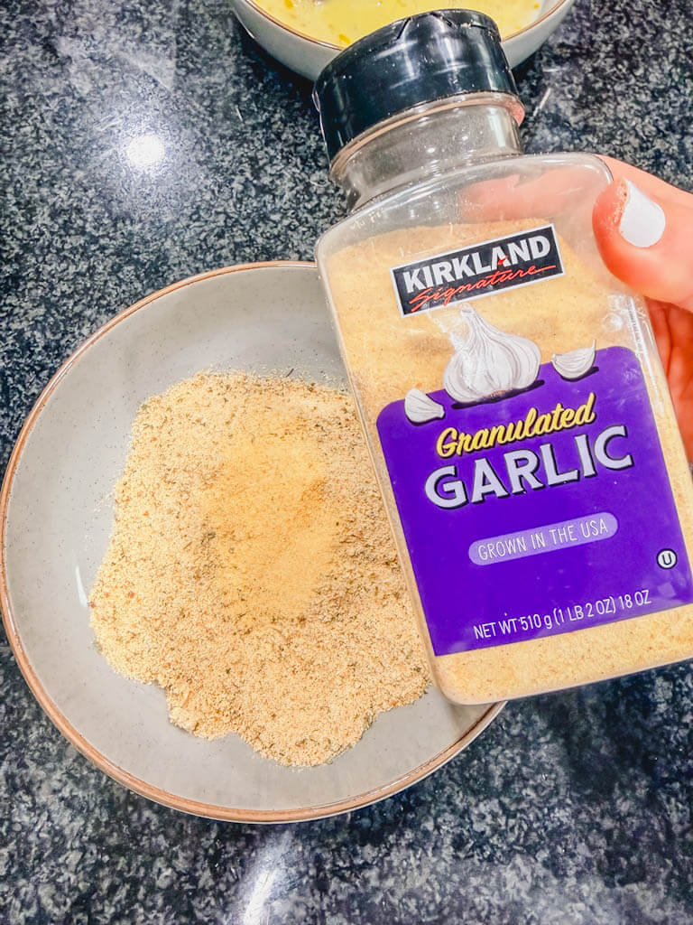 Garlic powder being added to the Italian breadcrumb mixture for oven fried chicken drumsticks.