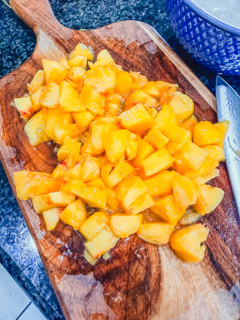 Fresh peaches peeled and diced on a wooden cutting board for homemade bakery-style peach streusel muffins.
