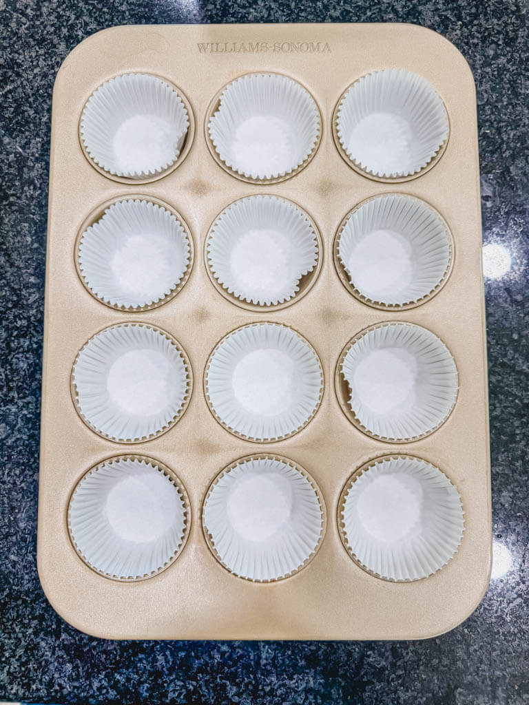 Muffin pan lined with paper liners and ready to be filled with peach muffin batter.