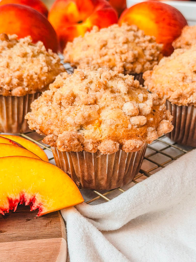 Up close shot of a fresh peach streusel muffin with sliced peaches next to the muffin.