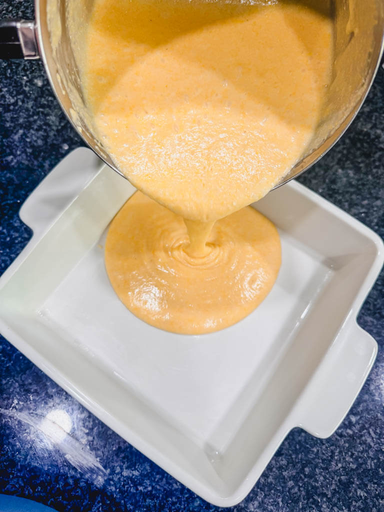 Sweet cornbread batter being poured into a greased 8x8 baking dish.
