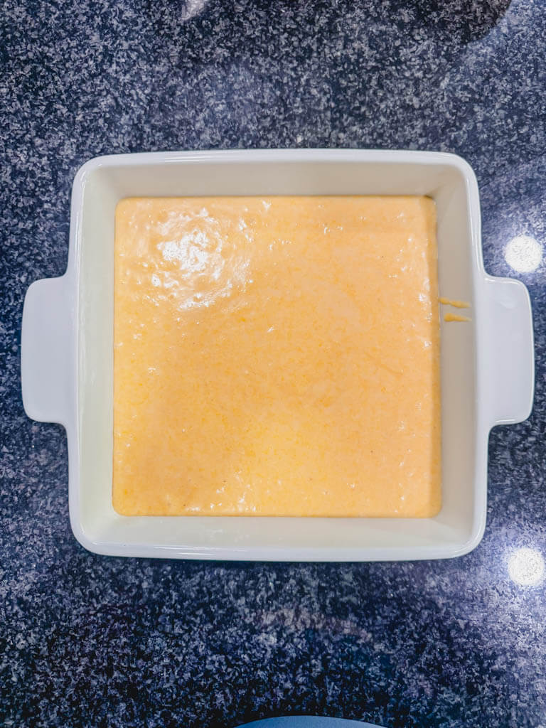 Cornbread batter evenly spread in an 8x8 baking dish before baking.