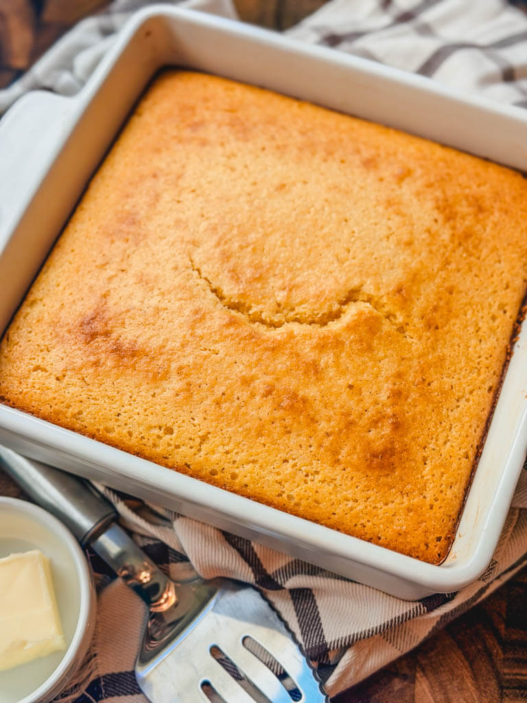 side view of cornbread next to a small bowl of butter and a serving utensil.