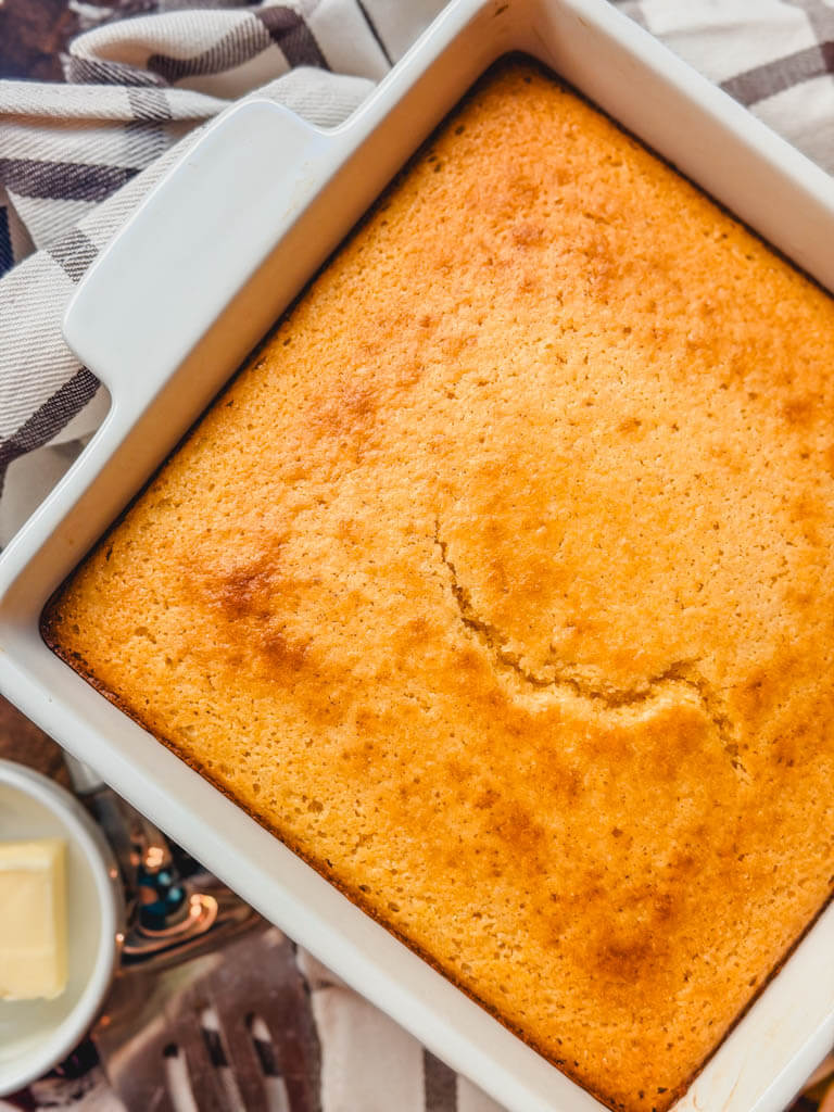 overhead view of cornbread in a white baking dish on top of a striped kitchen towel.