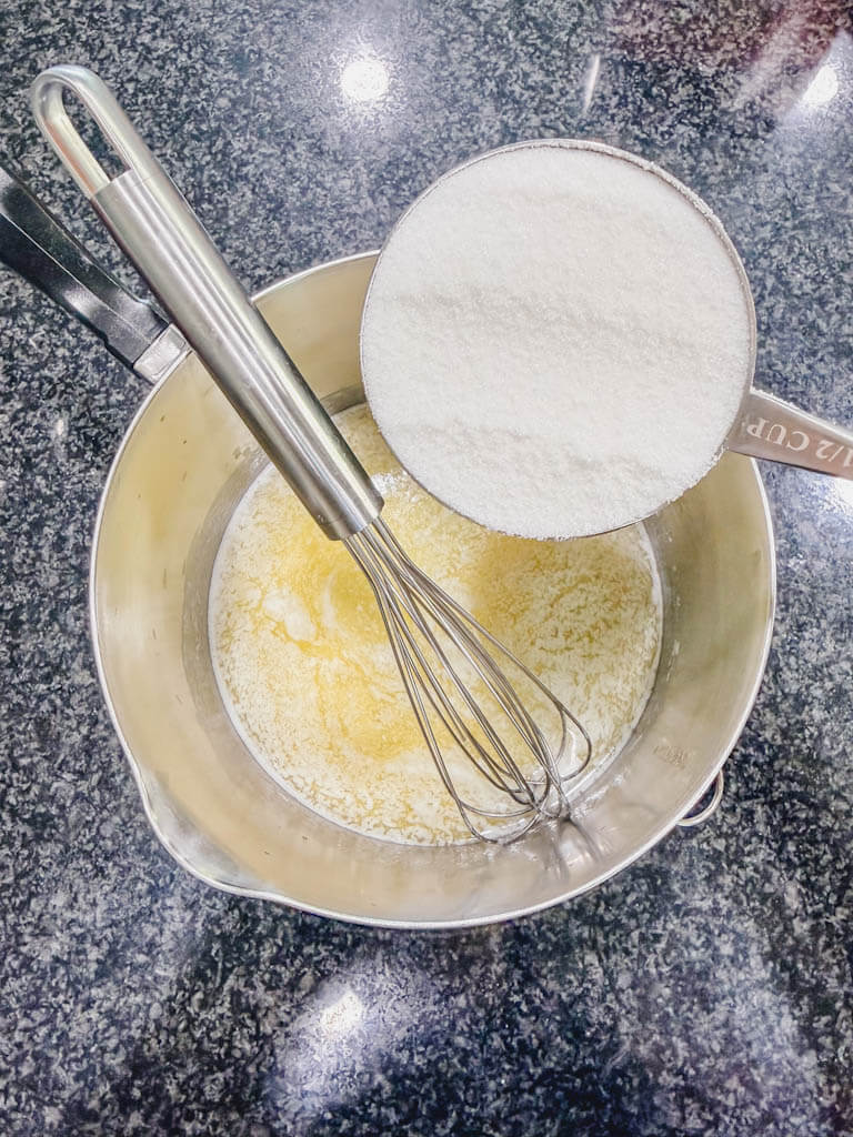 Granulated sugar being added to melted butter in a saucepan.