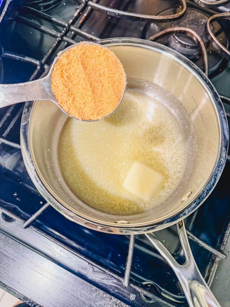 Brown sugar being added to melted butter in a saucepan for brown sugar Biscoff icing.