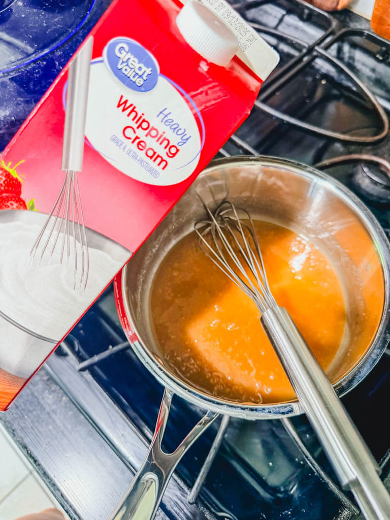 Heavy whipping cream being added to melted butter and brown sugar in a saucepan.