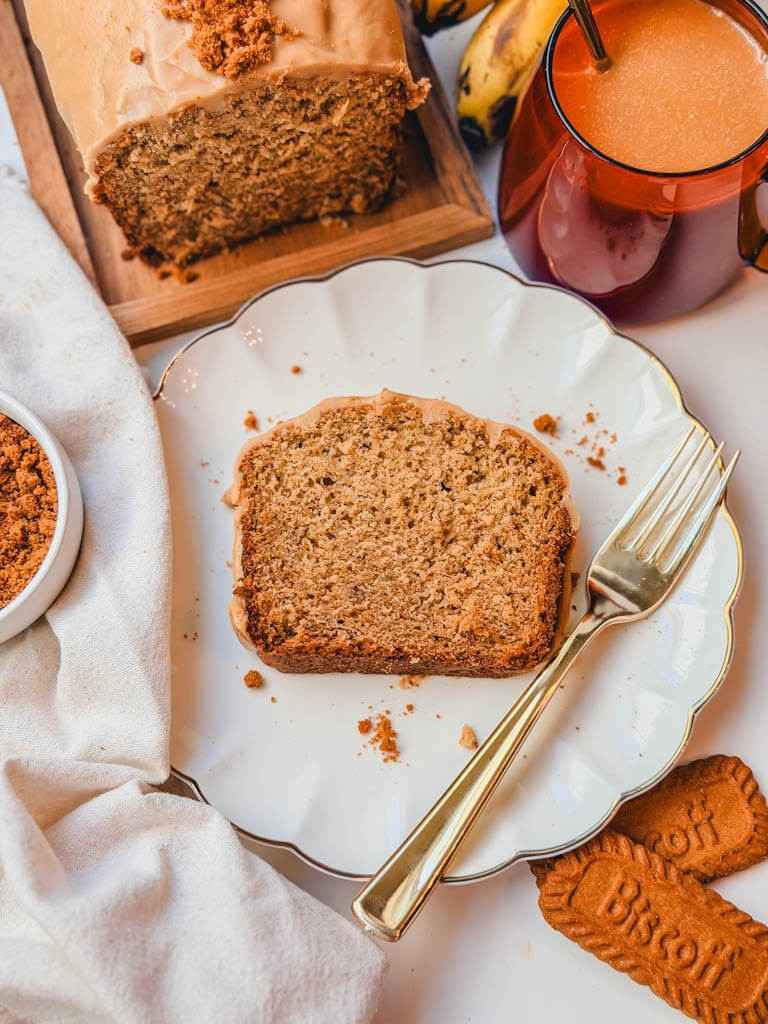 Overhead view of a slice of Biscoff banana bread on a white plate with Biscoff cookies and the loaf in the background.