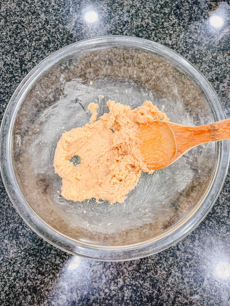 Butter and brown sugar creamed together in a glass mixing bowl with a wooden spoon.