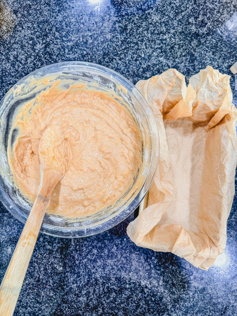 Biscoff banana bread batter beside a 9x5-inch loaf pan lined with crumpled parchment paper.