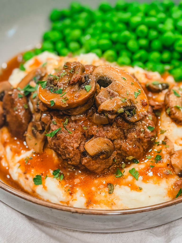 Instant Pot Salisbury steak with mushroom gravy served over creamy mashed potatoes with green peas.