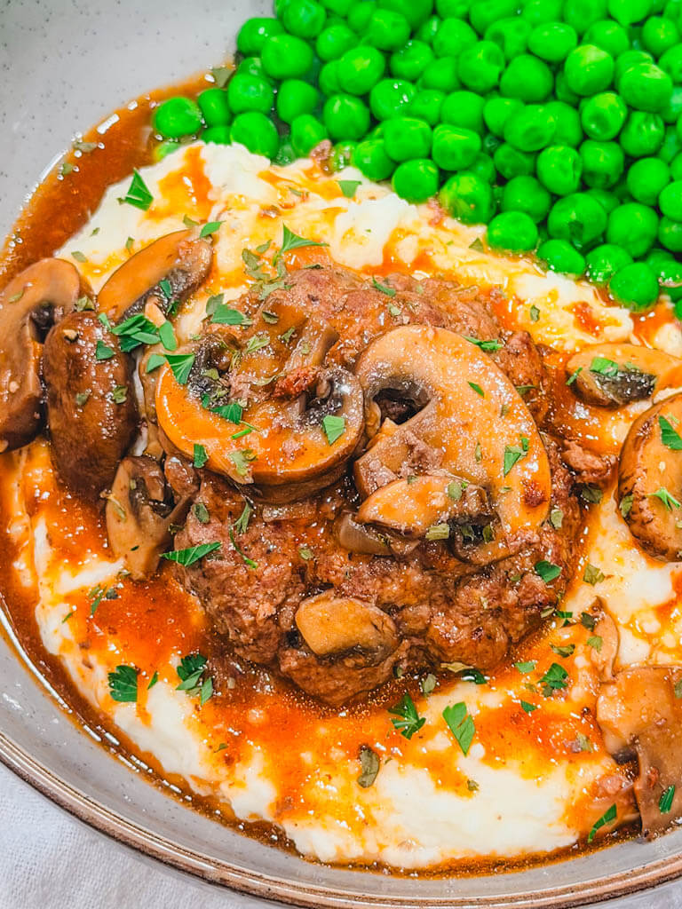 Easy Instant Pot Salisbury steak with mushrooms and gravy served with mashed potatoes and peas.