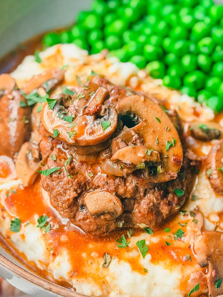 Close-up of Salisbury steak topped with mushrooms and rich gravy over mashed potatoes.