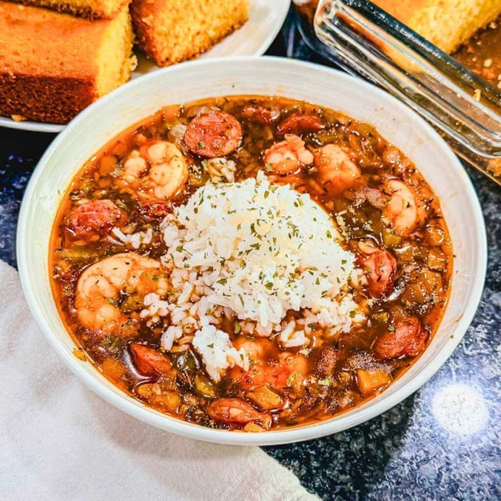 Shrimp and andouille sausage gumbo with vegetables and smoky sausage served in a white bowl topped with white rice.