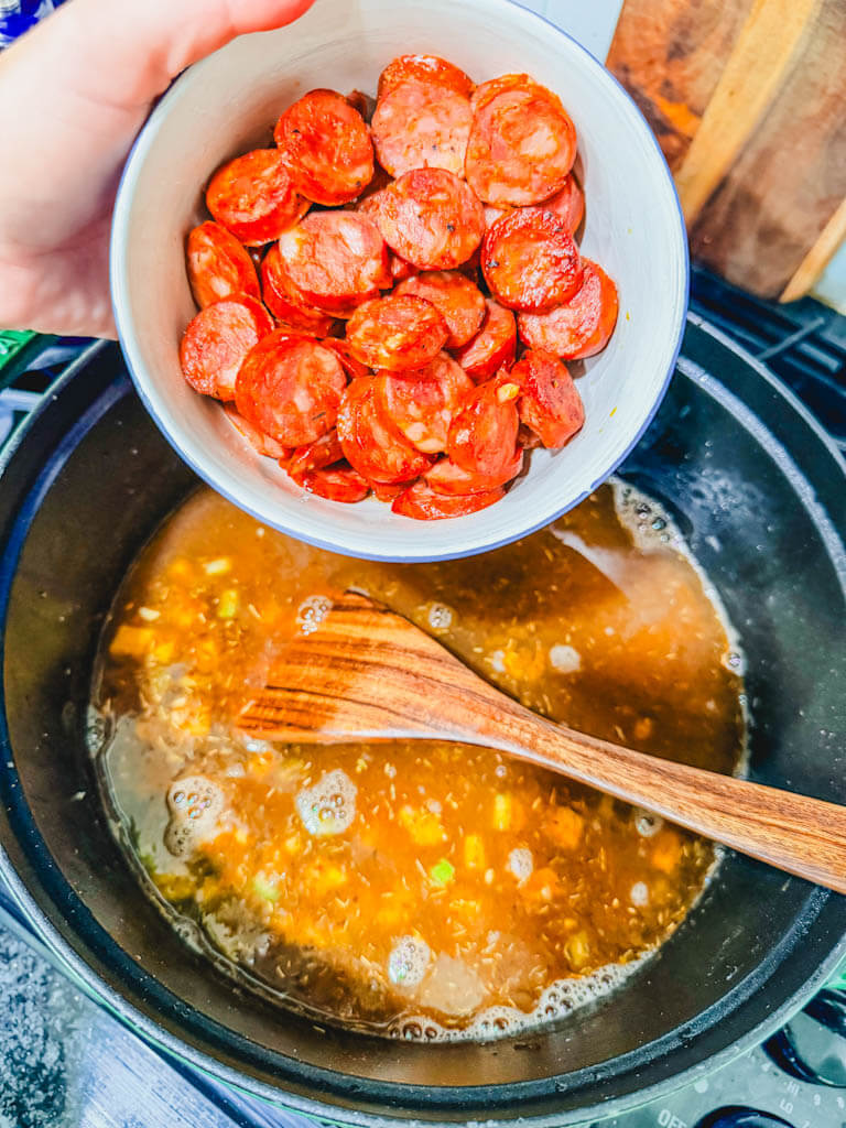 Browned andouille sausage being added back to gumbo in a Dutch oven.