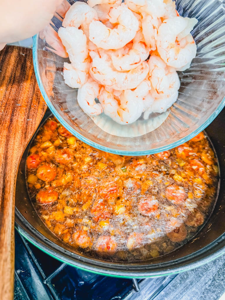 Raw peeled shrimp being added to andouille sausage gumbo near the end of cooking.