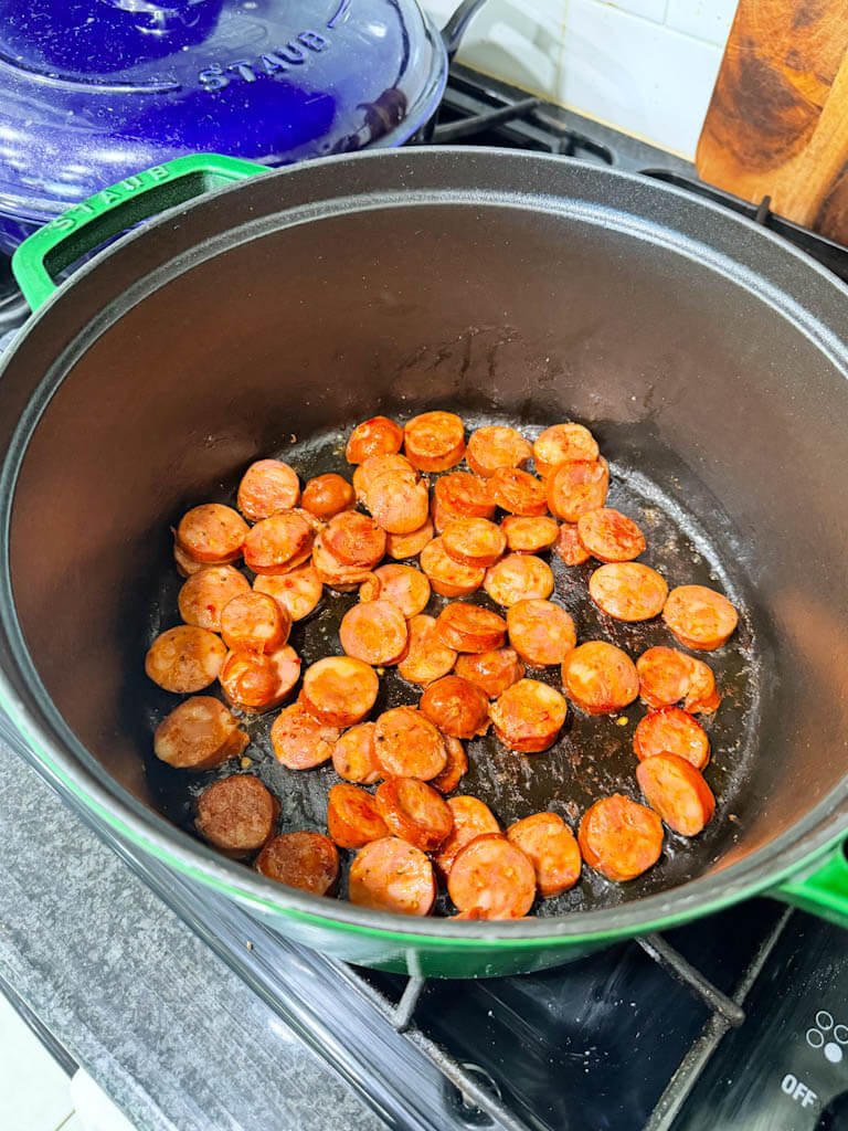 Sliced andouille sausage browning in a large Dutch oven.