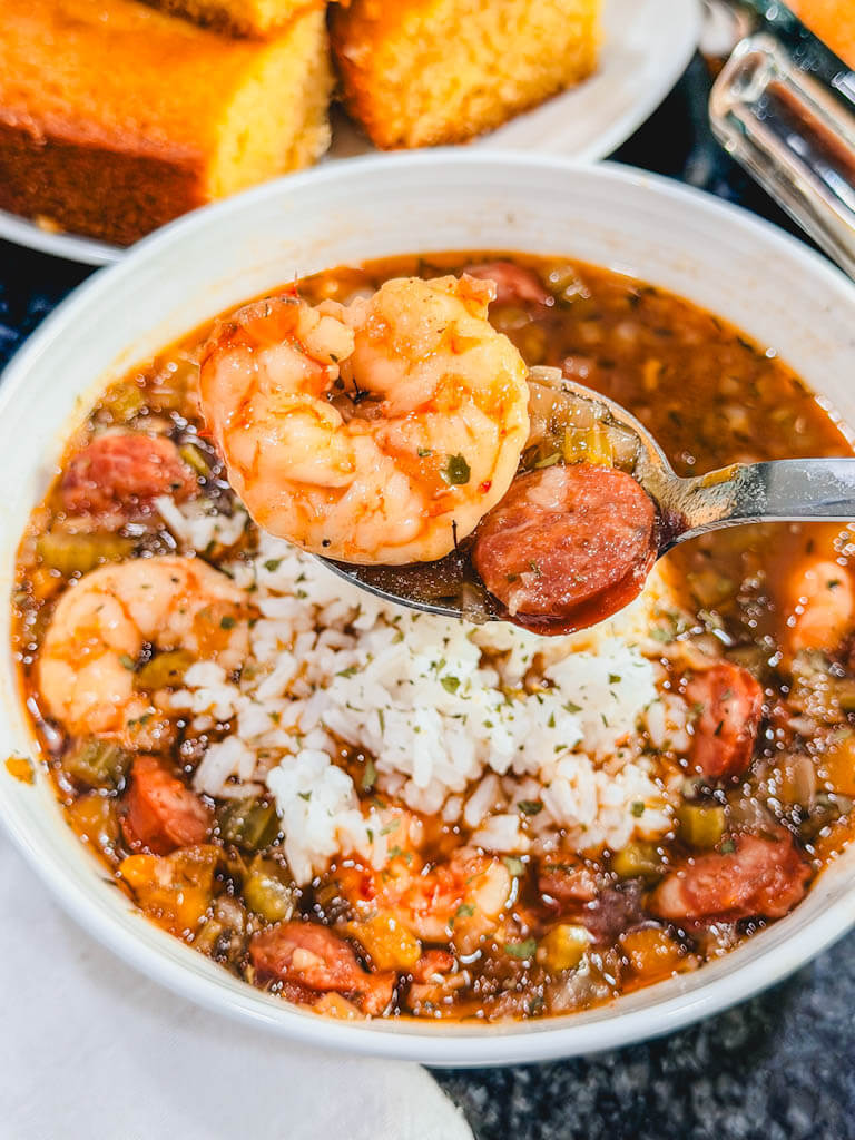 close up of shrimp and andouille sausage on a soup spoon being held over the bowl of gumbo.