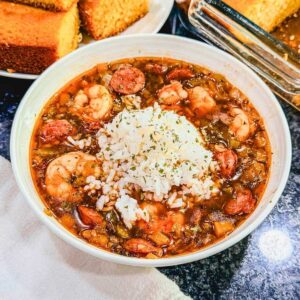 Shrimp and andouille sausage gumbo with vegetables and smoky sausage served in a white bowl topped with white rice.