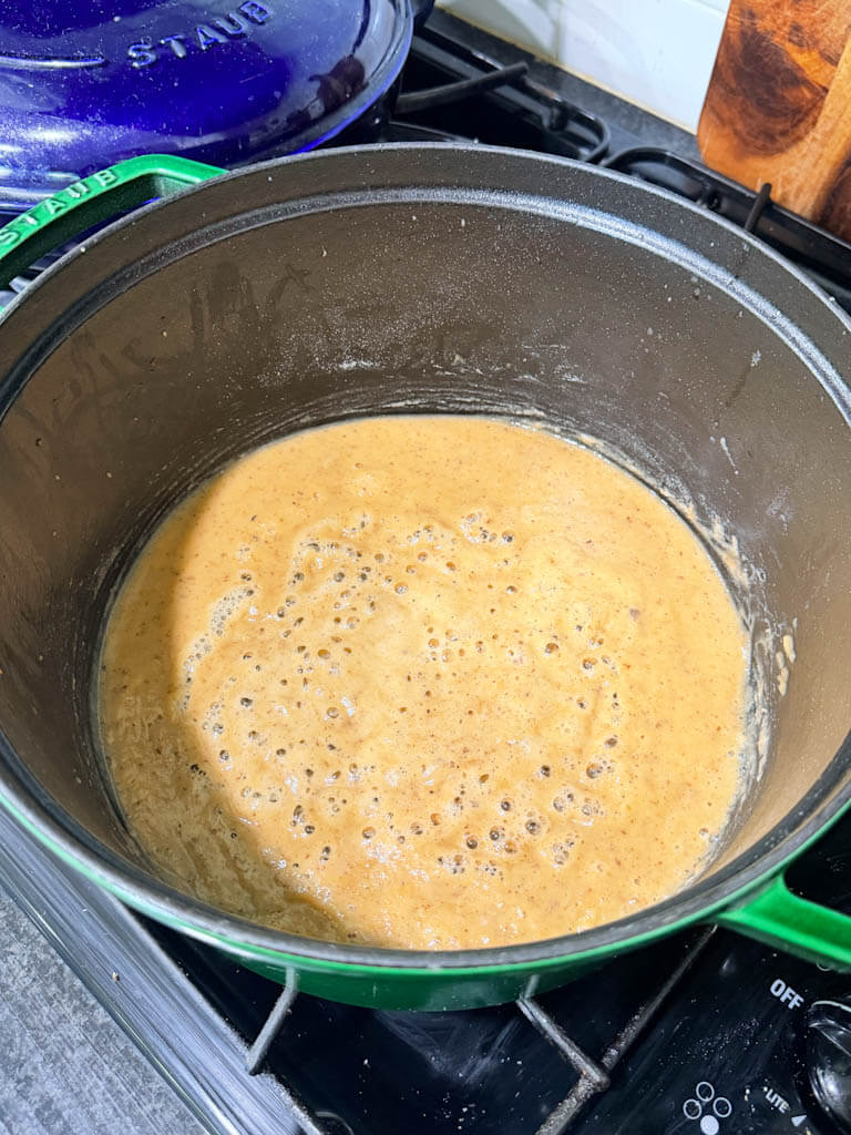 Light-colored gumbo roux bubbling in a Dutch oven during the early stage of cooking.