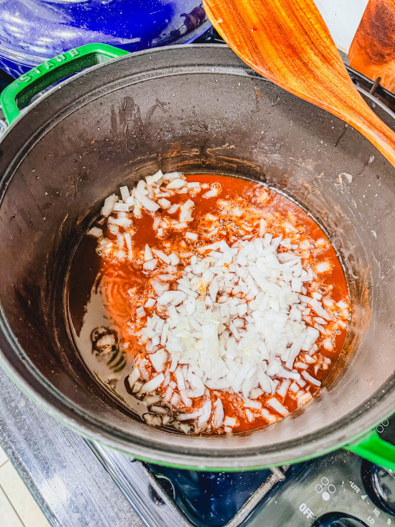 Diced white onion being added to dark brown gumbo roux.