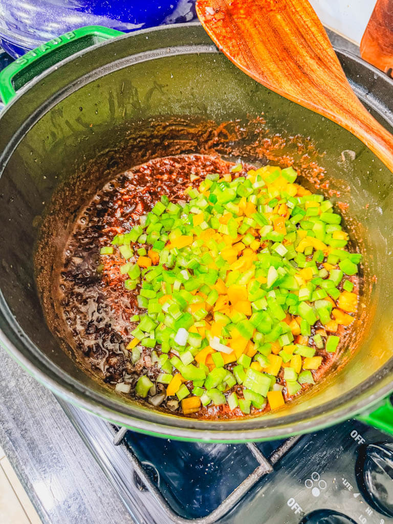 Diced celery and orange bell pepper added to onion and dark roux in a Dutch oven.